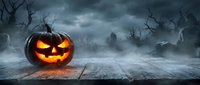 Glowing jack-o-lantern pumpkin on wooden table in spooky graveyard with bare trees and stormy sky. Halloween horror scene for seasonal decorations and marketing.