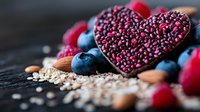 Heart-shaped dark chocolate with pink sprinkles surrounded by fresh blueberries, raspberries, almonds and oats on rustic wooden background. Perfect for healthy eating concept.