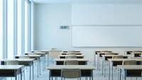 Modern classroom interior with rows of wooden desks and chairs facing whiteboard. Clean minimalist design with large windows providing natural light.
