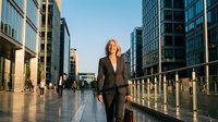 Mature woman in business suit walking through modern urban plaza with skyscrapers, professional corporate environment for executive, leadership, and career concepts.
