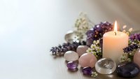 Healing crystals amethyst rose quartz with burning candle and dried flowers on white wooden surface for meditation wellness spa relaxation therapy.