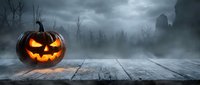 Glowing jack-o-lantern pumpkin on wooden table in spooky Halloween night scene with bare trees and misty atmosphere for seasonal decorations.