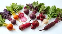 Fresh organic beetroot varieties with colorful roots and green leaves arranged on white background for healthy cooking and nutrition concepts.