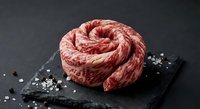 Raw ground beef formed into spiral shape on dark slate board with coarse salt and peppercorns for culinary preparation and cooking concepts.