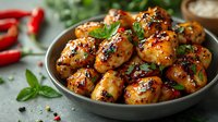 Glazed chicken wings with honey, soy sauce and sesame seeds garnished with fresh herbs and chili peppers in ceramic bowl on dark background. Asian cuisine.