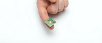 Close-up of a hand holding a small green computer microchip or processor against a white background, representing technology, innovation, and electronics.