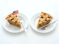Two slices of golden apple pie served on white plates with forks, one decorated with small American flag, isolated on white background for food design use.