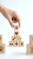 Hand placing wooden cube with paw print on pyramid of veterinary care symbols including heart, bone, stethoscope, medical cross and pet bed icons.