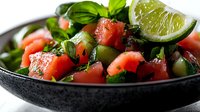 Fresh Mediterranean salad with diced tomatoes, olives, basil and lime wedge in dark bowl. Healthy vegetarian meal for restaurant menus and cooking blogs.