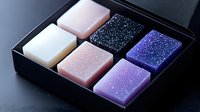 Glittering soap bars in black gift box featuring pastel pink, white, purple and blue colors with sparkly surface texture arranged in geometric pattern.