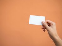 Caucasian hand holding blank white business card against warm orange background, suitable for branding, marketing materials, and corporate presentations.