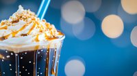 Caramel frappuccino topped with whipped cream and drizzle against blurred blue bokeh background, sweet cold coffee drink with cream and sauce.