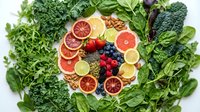Fresh organic vegetables and colorful citrus fruits arranged in circular pattern surrounded by leafy greens for healthy eating and nutrition concepts.