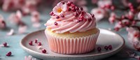 Pink frosted vanilla cupcake decorated with pomegranate seeds on ceramic plate against blurred floral background, soft pastel colors create romantic mood.