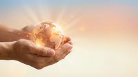Hands gently holding glowing Earth globe with warm sunlight rays against soft sky background symbolizing environmental protection and global responsibility.