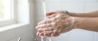 Hands washing with soap and water in bathroom sink, proper hygiene routine for health and cleanliness prevention.