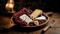 Red grapes, cheese, and figs arranged on wooden board with vintage oil lamp, ideal for food styling, culinary content, and gourmet still life compositions.