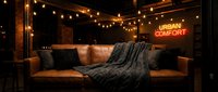 Warm-toned lounge setting with cognac leather sofa, decorative pillows, draped throw blanket, string lights, and neon sign for hospitality, interior design, and lifestyle marketing.