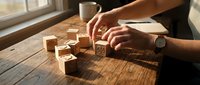 Hands arranging wooden alphabet blocks on rustic table near window with warm sunlight and coffee cup creating cozy learning atmosphere.