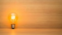 Glowing vintage light bulb with warm yellow illumination against wooden background, creating minimalist atmosphere for creative concept designs.