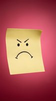 Yellow sticky note with angry sad face drawing on pink gradient background expressing negative emotions and frustration for office communication.