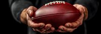 Panoramic view of male hands holding professional football against dark background, dramatic lighting emphasizes leather texture and game ball details.