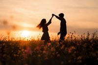Romantic couple silhouettes dancing in wildflower meadow at golden sunset. Love, relationship and togetherness concept for wedding invitations.