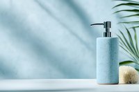 Minimalist blue soap dispenser on white surface with palm leaf shadow and natural sponge. Trendy bathroom accessories for modern spa and wellness interior.
