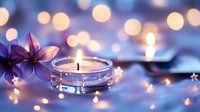 Glowing candle in glass holder with purple flowers against blurred bokeh lights background creates peaceful spa atmosphere for wellness design.