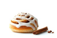 Fresh cinnamon roll with white vanilla glaze drizzle and aromatic cinnamon sticks on white background, isolated pastry for bakery and food design.