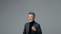 Mature man with gray hair and beard, wearing dark blazer over black turtleneck, isolated against neutral gray background. Suitable for corporate, business, professional, and lifestyle marketing materials.