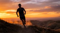 Male athlete jogging on mountain trail at golden sunset, silhouetted against dramatic orange sky. Trail running, fitness, outdoor sports.