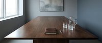 Modern wooden conference table in minimalist office meeting room with blue walls and natural lighting for business presentations.
