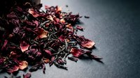 Dried hibiscus flowers and tea leaves mixed together on dark surface for beverage preparation and herbal wellness.