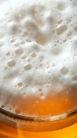 Closeup of golden beer with thick white foam head and bubbles in glass, ready for beverage, brewery, and pub design projects.
