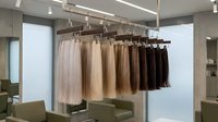 Hair extensions in various shades hanging on display rack in modern salon interior with professional lighting and mirrors for beauty treatments.
