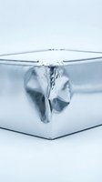 Shiny silver metallic gift box with reflective foil wrapping and ribbon bow on white background for holiday celebrations and special occasions.