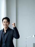 Asian male professional in dark navy shirt making fist pump gesture against white wall background, expressing success and motivation for business, corporate, and achievement concepts.