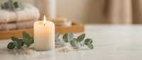 Burning white candle with eucalyptus leaves on marble surface creating peaceful spa atmosphere for relaxation and wellness rituals.