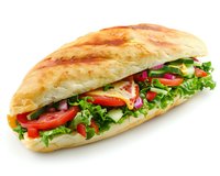Fresh submarine sandwich with crisp lettuce, sliced tomatoes, red onions, cucumbers, and cheese on crusty baguette bread, isolated on white background for menu design.
