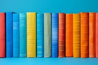 Row of colorful hardcover books standing on shelf against bright blue background, spines showing various sizes and textures in orange, yellow and blue tones.