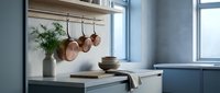 Modern kitchen interior with copper pots hanging from wooden rail, blue cabinets and natural light creating cozy cooking space atmosphere.
