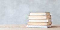 Stack of white and beige hardcover books on wooden table against light gray wall background, minimalist composition for education and reading concepts.