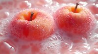 Two red apples covered in frost and ice crystals, glistening with water droplets against a soft pink bokeh background. Fresh produce and winter themes.