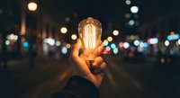 Hand holding glowing vintage Edison bulb against blurred city lights at night creating warm atmospheric lighting for creative concepts and innovation themes.