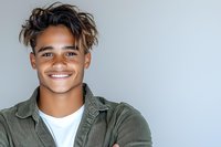 Young mixed race man with bright smile wearing olive green corduroy shirt and white t-shirt against light background, arms crossed in confident pose.