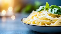 Fresh fettuccine pasta garnished with basil leaves in ceramic bowl on blue background with soft bokeh lights, close up view for restaurant menu design.