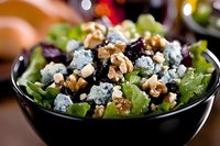 Fresh green salad with crumbled blue cheese, walnuts, and dried cranberries served in black ceramic bowl, close up view on wooden table with soft bokeh background.