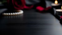 Romantic dark wooden surface with red roses, pearl necklace and candles creating elegant Valentine's Day or anniversary atmosphere for luxury product display.