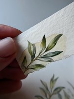 Delicate watercolor olive branch on textured paper with soft yellow background, held by fingers. Perfect for wedding stationery or botanical designs.